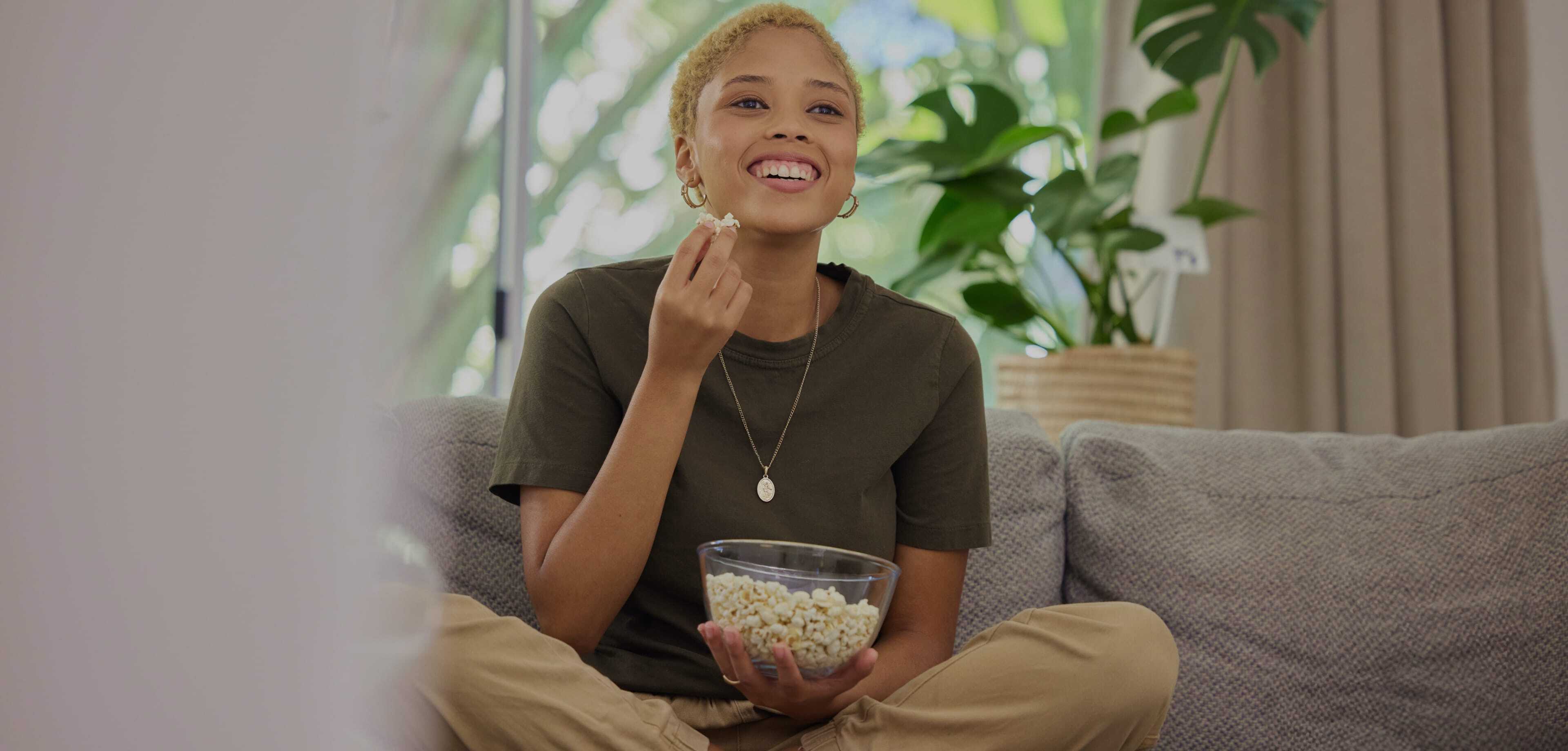 femme souriante mangeant du popcorn sur un canapé